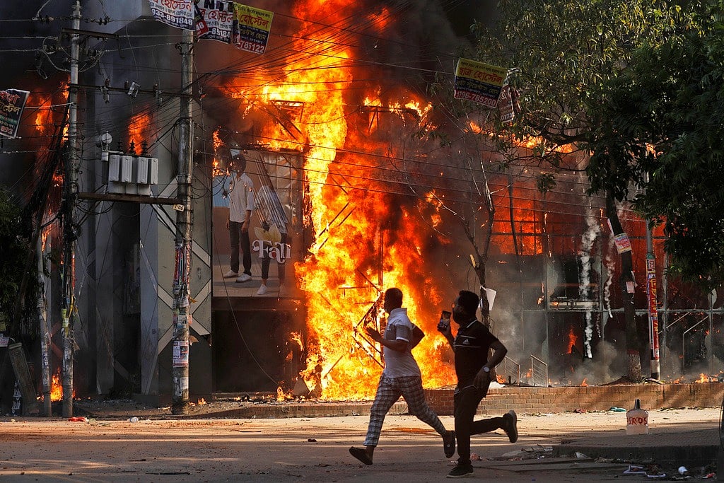 AP : Men run past a shopping centre which was set on fire by protesters during a rally against Prime Minister Sheikh Hasina
